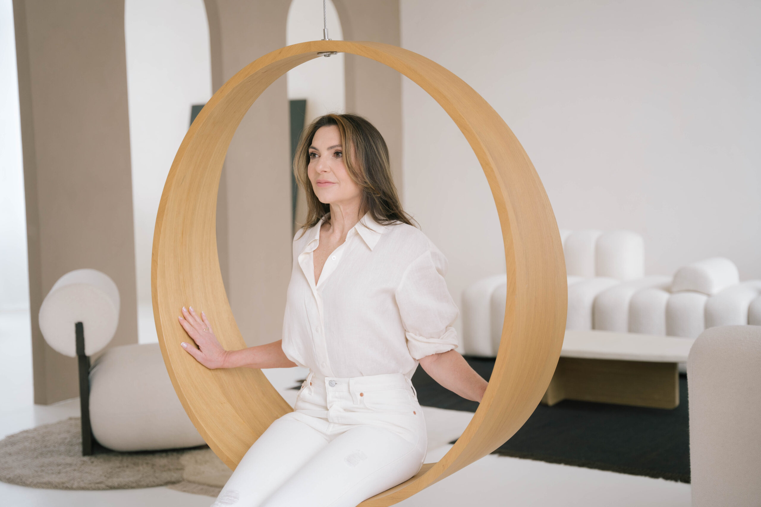 Marjena in witte blouse en witte broek op een moderne schommelstoel