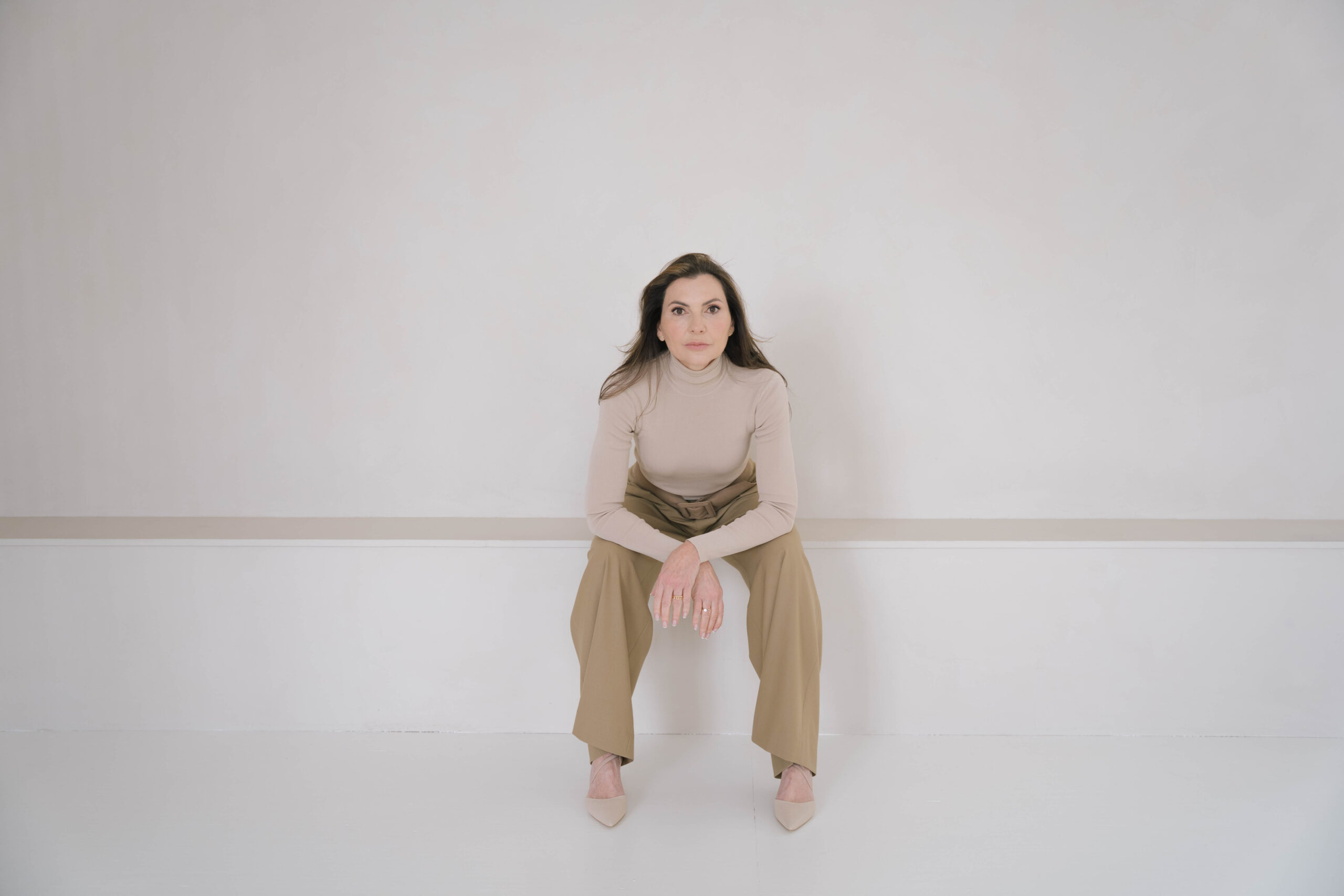 Marjena in de studio zittend, ellebogen op haar knieën. Serieus kijken