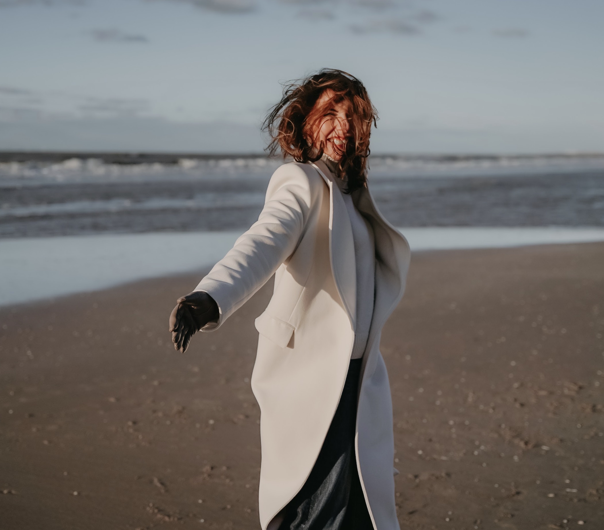 Marjena op het strand in een witte herfstjas